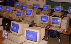 there are many computers on the desks in this class room, all with blue screens