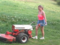 a woman standing next to a red and white lawn mower on top of a lush green field