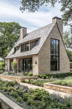 a stone house with lots of windows and plants in the front yard, surrounded by greenery