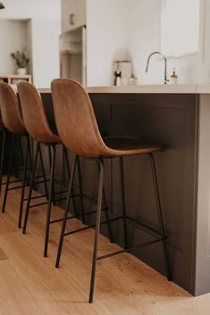 three brown bar stools sitting in front of a kitchen counter with an island and sink