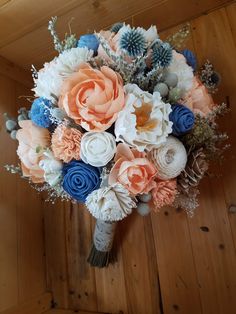 a bridal bouquet with peach, blue and white flowers on a wooden floor in a room