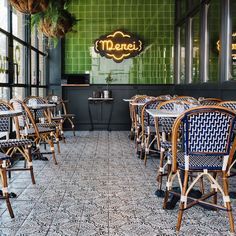 the interior of a restaurant with green tiled walls and wooden chairs, plants hanging from the ceiling