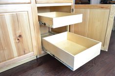 an open drawer in the middle of a kitchen with wood floors and cabinets behind it