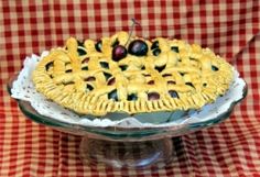 a pie sitting on top of a glass cake plate next to a red and white checkered table cloth