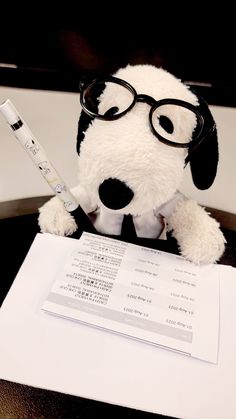 a stuffed dog wearing glasses sitting on top of a desk next to a pen and paper