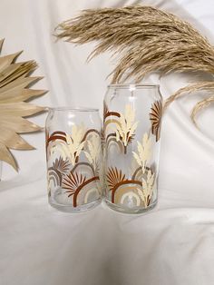 two glasses sitting next to each other on a white surface with dried grass in the background