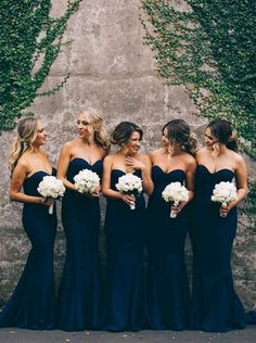 a group of women standing next to each other in front of a wall with ivy growing on it