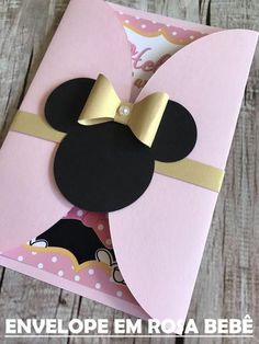 a pink card with a gold bow and mickey mouse on it's head in front of a wooden background