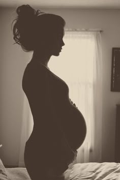 a pregnant woman standing on top of a bed next to a white curtain and window