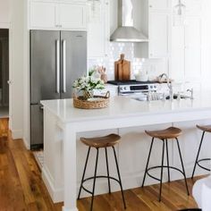 a white kitchen with three stools and a center island in the middle of the room