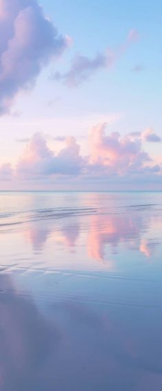 two people walking on the beach with their surfboards in hand and clouds reflected in the water