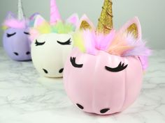 three plastic unicorn pumpkins sitting on top of a white marble counter topped with pink, yellow and green decorations