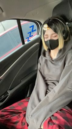 a woman with headphones sitting in the back seat of a car wearing a hoodie