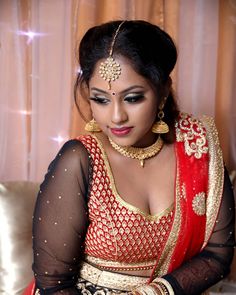 a woman in a red and gold bridal outfit sitting on a couch with her hands together