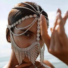 a woman wearing an elaborate head piece with chains and jewels on her face, in front of the ocean