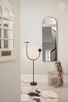 a white room with a mirror and a black lamp on the floor in front of it