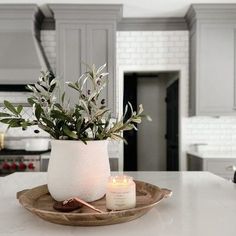 a candle is sitting on a plate in the middle of a kitchen counter with an olive plant