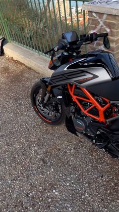 an orange and black motorcycle parked next to a fence