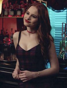 a woman standing in front of a bar wearing a black and red dress with her hands on her hips