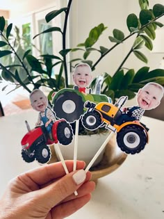 a person holding up some cake toppers with pictures of people on them in front of a potted plant