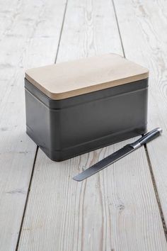 a black box with a wooden lid sitting on top of a white wood floor next to a pair of scissors