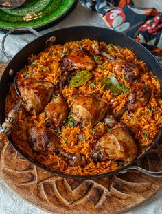 a pan filled with chicken and rice on top of a wooden cutting board