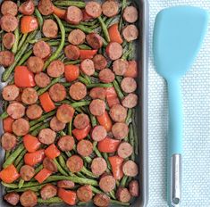 a pan filled with green beans, carrots and sausage next to a spatula