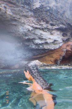 a woman swimming in the water near a cave with steam coming out of it's mouth