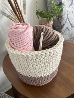 two crocheted baskets with yarn and plants in them on a table next to pillows