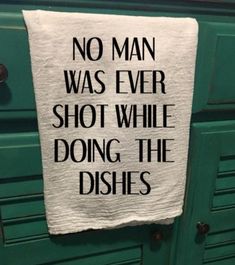 a tea towel hanging on the side of a green cabinet that says, no man was ever shot while doing the dishes