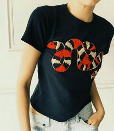 a woman wearing a t - shirt with a snake on it's chest, standing in front of a white wall