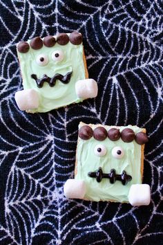 two decorated cookies with green frosting and chocolate eyes on a spider web tablecloth