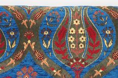 a blue, red and gold patterned pillow with flowers on the front side is shown