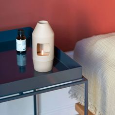 a white vase sitting on top of a glass table next to a bottle with a candle in it