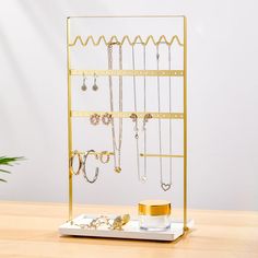 a gold jewelry rack with earrings, bracelets and rings on it next to a potted plant