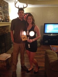 a man and woman standing next to each other in front of a fireplace with deer antlers on it