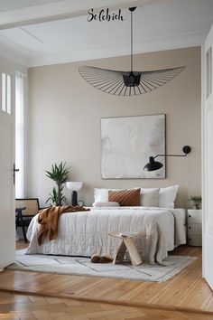 a bedroom with white walls and wood flooring has a large painting on the wall