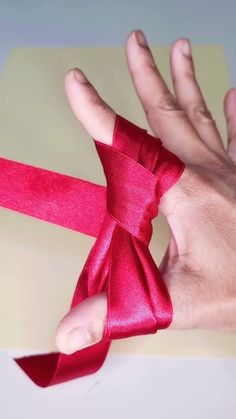 a hand holding a red ribbon on top of a piece of paper that has been folded