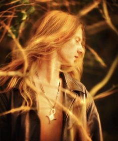 a woman with long hair is standing in front of some branches and looking off into the distance