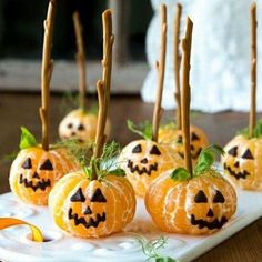 small pumpkins with sticks sticking out of them sitting on a white plate next to green leaves