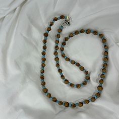 a blue and brown beaded necklace laying on top of a white cloth covered bed