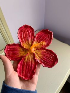 a person holding up a red flower in front of a white dresser with purple walls