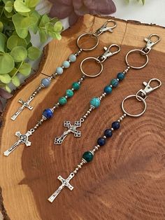 three cross keychains with beads and charms on a wooden board next to flowers