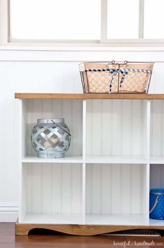 a white shelf with some baskets on top of it next to a blue and white vase