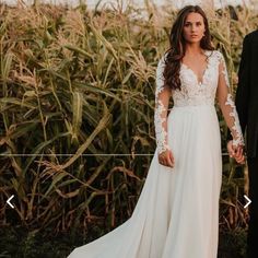 a man and woman standing next to each other in front of a corn field holding hands