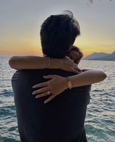 two people embracing each other while standing in front of the ocean