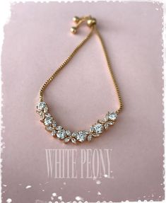 a gold bracelet with white stones is shown on a light pink background and says white peony