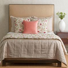 a bed with pink and white pillows on top of it next to a night stand