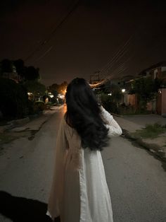 a woman walking down a street at night with her hair blowing in the wind and wearing a veil