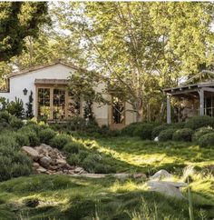 the house is surrounded by lush green grass and rocks, with trees in the background